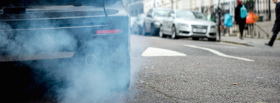 close-up image of car's exhaust pipe and heavy fumes next to people crossing street