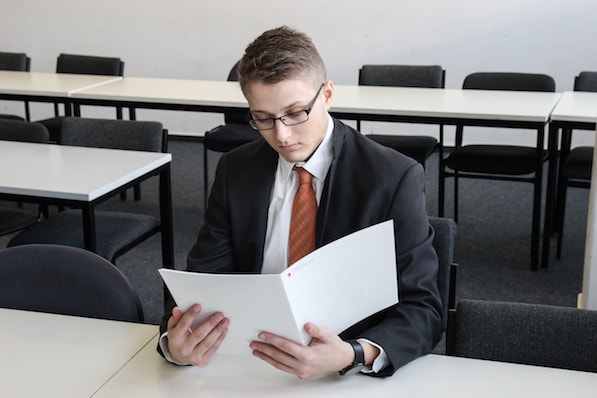 young man in tie and suit, sitting in empty classroom studying accounting questions